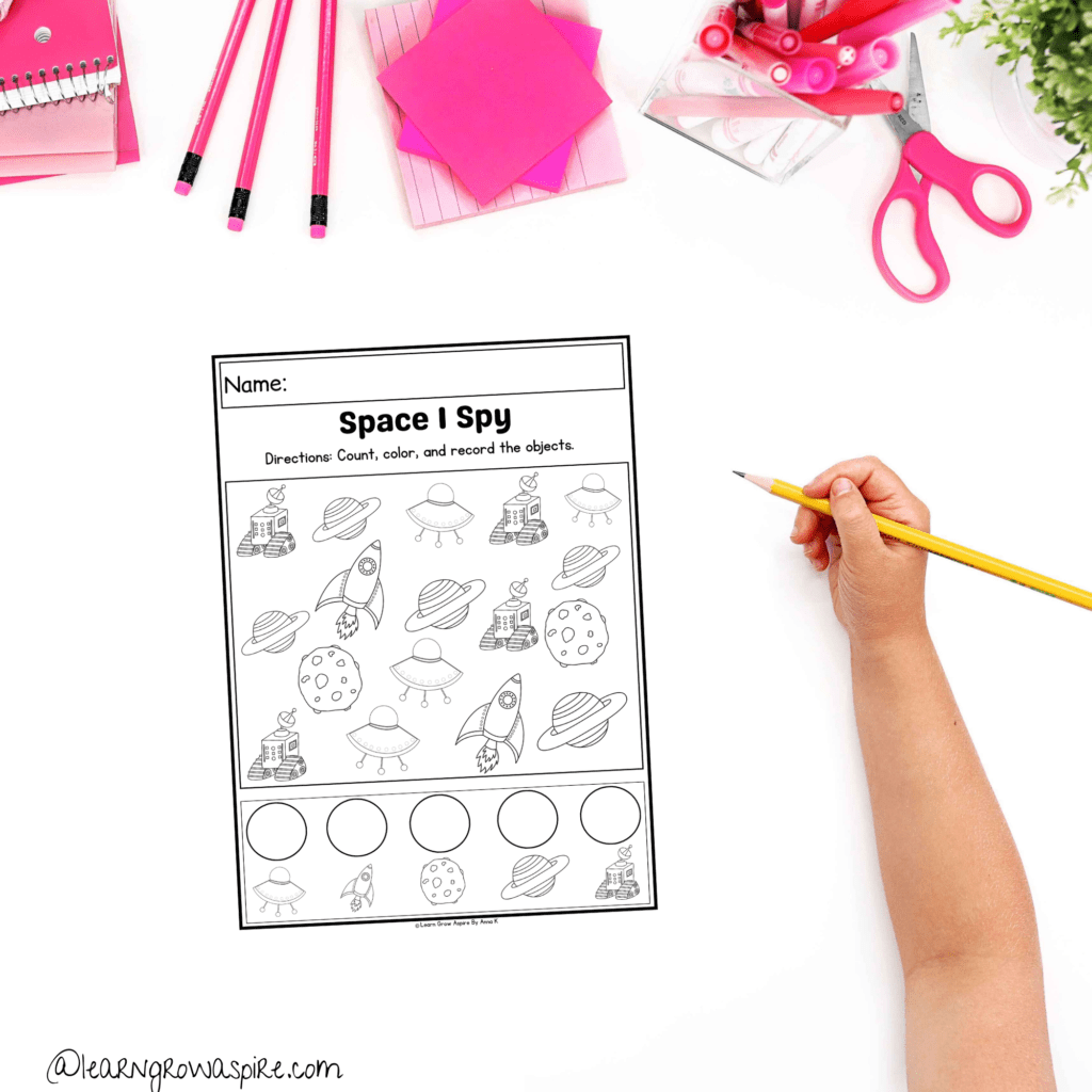 A child hand holding a pencil working on their space I spy printable. Space i spy printable for preschoolers pdf free download.